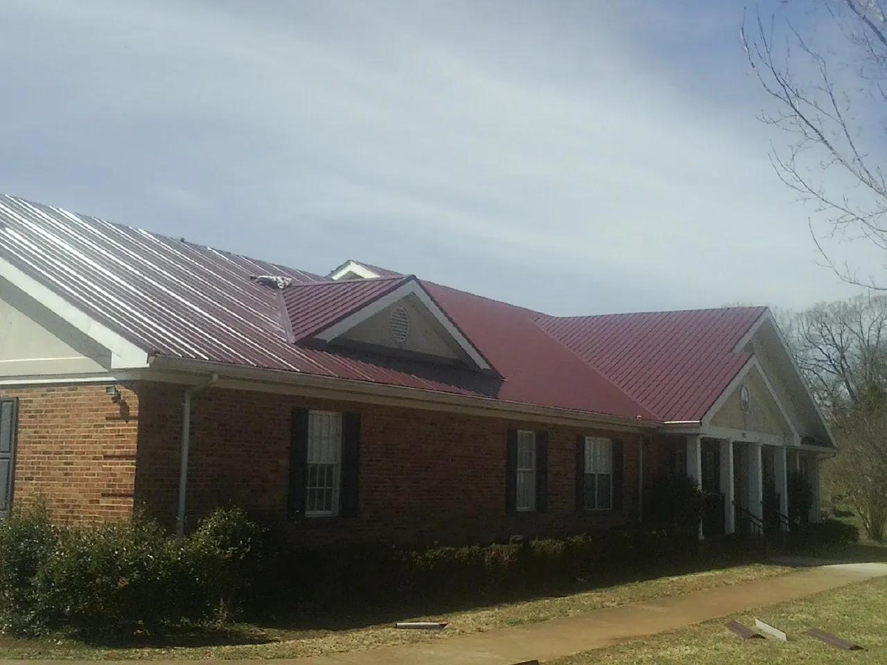 Red metal roof with gabled entries on a long brick building, from a Hail Damage Roof Repair job in Adena