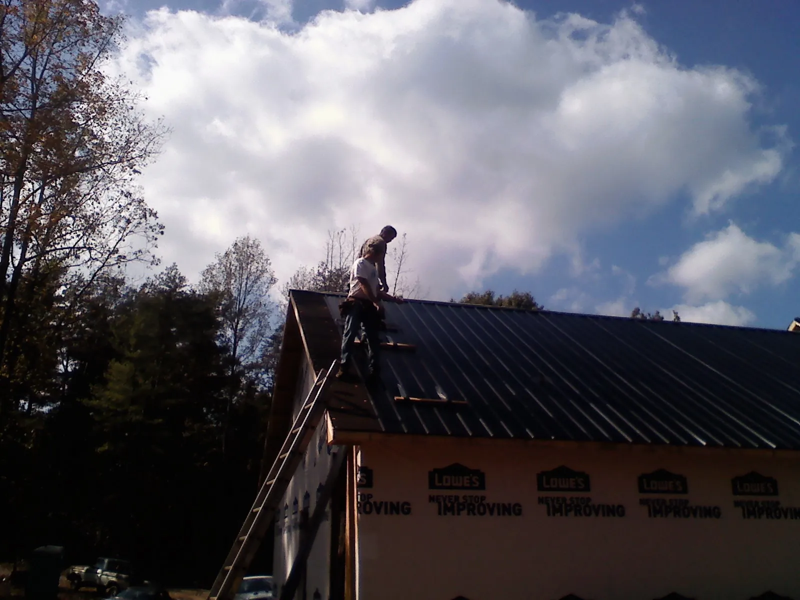 Roofer fastening dark metal panels high against a cloudy sky, from a Roof Inspection job in Adena